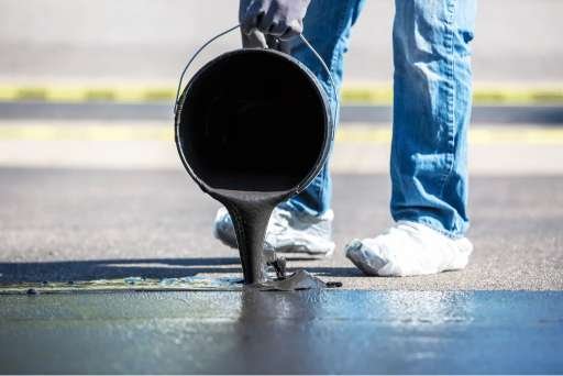 pouring liquid bitumen sealer onto asphalt surface for driveway sealing