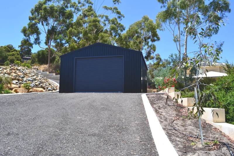Modern black metal garage shed at the end of a gravel driveway