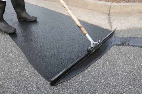Applying fresh black sealcoat liquid onto an asphalt pavement